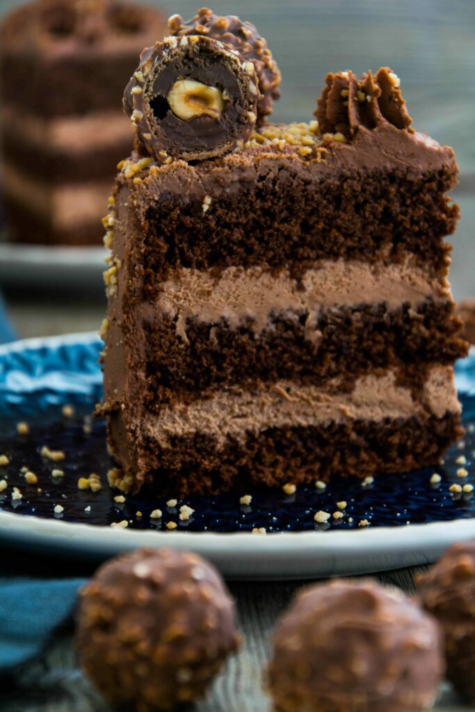 Seitenansicht von einem Stück Schokoladen-Nusstorte mit einer angeschnittenen Ferrero Rocher Kugel verziert